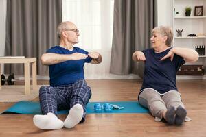 Senior couple doing back exercises sitting on yoga mat. Old person healthy lifestyle exercise at home, workout and training, sport activity at home. photo