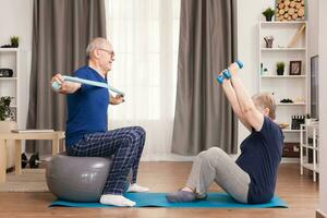 Pensioners doing sport in pajamas with resistance band and dumbbells. Old person healthy lifestyle exercise at home, workout and training, sport activity at home on yoga mat. photo