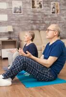 Retired people meditating on yoga mat in living room. Old person healthy lifestyle exercise at home, workout and training, sport activity at home on yoga mat. photo