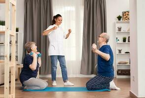 Doctor encouraging his patients to exercise for recovery. Home assistance, physiotherapy, healthy lifestyle for senior old person, training and recovery with professional physiotherapist using dumbbells, resistance band and yoga mat. photo