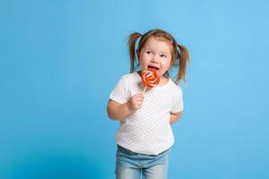 Beautiful little female child holding huge lollipop spiral candy smiling happy isolated on blue background. photo