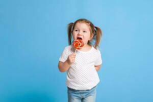 Beautiful little female child holding huge lollipop spiral candy smiling happy isolated on blue background. photo