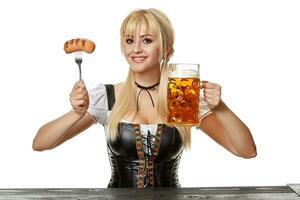 Young bavarian woman in dirndl sitting at table with beer on white background photo