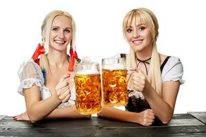 Two beautiful women holding a glass of beer while sitting at a wooden table on a white background in the studio photo
