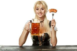 Young bavarian woman in dirndl sitting at table with beer on white background photo