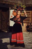 Brunette girl in a black and red ukrainian embroidered authentic national costume and a wreath of flowers is posing standing at the gate. photo