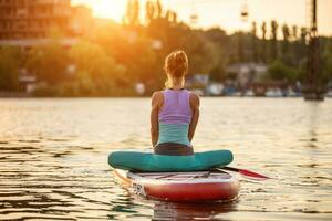 Young woman doing yoga on sup board with paddle. Yoga pose, side view - concept of harmony with the nature. photo