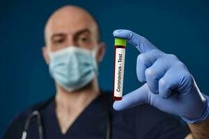 médico en mascarilla, azul guantes, médico uniforme. participación rojo laboratorio prueba tubo en mano. azul antecedentes. coronavirus, COVID-19. cerca arriba foto