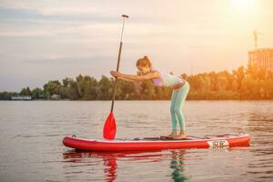 Sporty woman in yoga position on paddleboard, doing yoga on sup board, exercise for flexibility and stretching of muscles photo