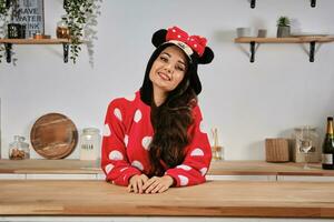 Woman dressed up in red plush pajama in form of cartoon character mouse is having fun at hen-party. She is smiling, sitting at a wooden kitchen table. photo