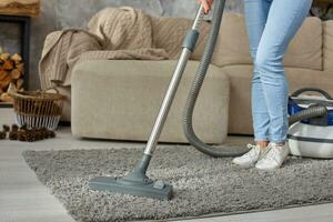 recortado imagen de hermosa joven mujer utilizando un vacío limpiador mientras limpieza alfombra en el casa foto