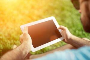 Young man using and typing tablet computer in summer grass. photo