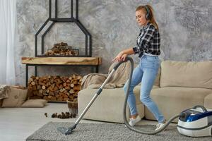 Full length portrait of cheerful young woman 20s listening to music via headphones and having fun with vacuum cleaner in the house. photo