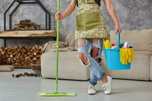 Cleaning service. Bucket with sponges, chemicals bottles and mopping stick. Cropped image of a woman with a mop at the living room photo