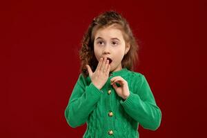 Portrait of a little brunette girl with a long, curly hair posing against a red background. photo