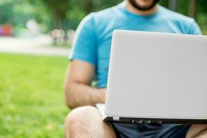 Young man using and typing laptop computer in summer grass. photo