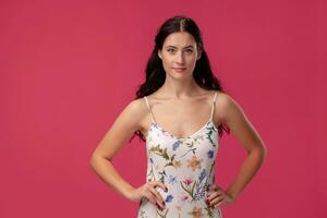 Portrait of a pretty young woman in a light dress standing on pink background in studio. People sincere emotions. photo