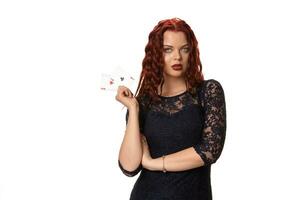 joven mujer con un largo rojo pelo en noche atuendo, participación jugando tarjetas aislado en blanco. póker foto