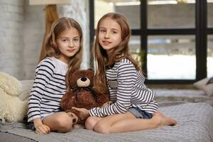 el imagen de dos pequeño hermanas sentado en el cama en el habitación. foto