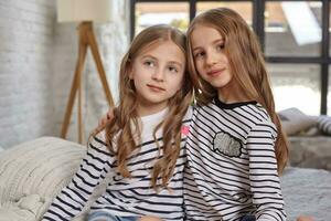 The image of two little sisters sitting on the bed in the room. photo
