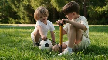 zwei Kinder von heiter freunde aufblasen ein Fußball Ball mit ein Pumpe. video