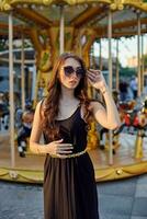 Portrait of a beautiful brunette woman in evening dress next to a children's carousel. photo