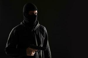 The robber in a mask with a gun pointed to the side on a black background photo