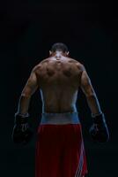 posterior ver de fuerte joven masculino Boxer. aptitud masculino modelo vistiendo boxeo guantes en pie en negro antecedentes. foto