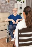 Nurse consulting an old man in wheelchair sitting in the living room. Disabled disability old person with medical worker in nursing care home assistance, healthcare and medicine service photo