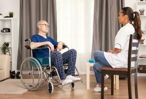 Person in whellchair talking with nurse in the doctor's office. Disabled disability old person with medical worker in nursing care home assistance, healthcare and medicine service photo