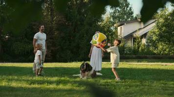 A cheerful family of four and a dog are playing on the lawn near the house. video