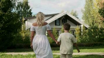 Happy mom and son are walking on the grass on the lawn near the house. video