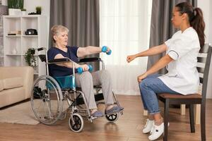 Senior woman in wheelchair doing rehab with weights. Disabled handicapped old person recovering professional help nurse, nursing retirement home treatment and rehabilitation photo