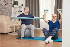 Senior couple exercising at home toning their arms. Old person healthy lifestyle exercise at home, workout and training, sport activity at home on yoga mat. photo