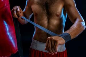 Boxer preparando su guantes para un luchar. foto de muscular hombre fornido arriba manos en negro antecedentes.