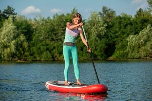 Woman is floating on a SUP board on sunny morning. Stand up paddle boarding - awesome active recreation during vacation. photo