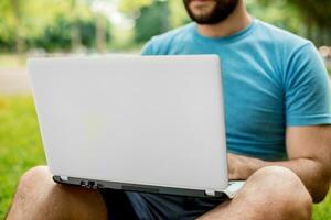 joven hombre utilizando y mecanografía ordenador portátil computadora en verano césped. foto