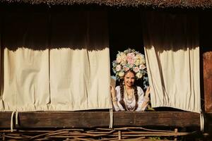 Brunette girl in a white ukrainian authentic national costume and a wreath of flowers is is looking out of the window. photo