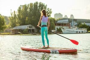 Woman is floating on a SUP board on sunny morning. Stand up paddle boarding - awesome active recreation during vacation. photo