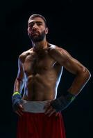 Handsome athletic guy in a red shorts on a black background. The boxer is fetching his breath after practicing hooks and blows. photo