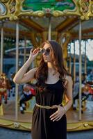 Portrait of a beautiful brunette woman in evening dress next to a children's carousel. photo