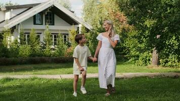 Happy mom and son are walking on the grass on the lawn near the house. video