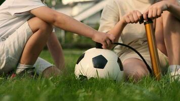 zwei Kinder von heiter freunde aufblasen ein Fußball Ball mit ein Pumpe. video