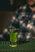 Shot glass with layered drink Green Mexican on bar counter photo
