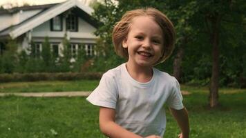 un alegre niño carreras y sonrisas a través de el césped cerca el casa. video