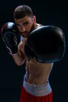 Portrait of tough male boxer posing in boxing stance against black background. photo