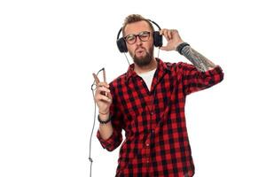 joven hipster hombre en a cuadros camisa y lentes vistiendo auriculares mirando contento en blanco antecedentes. foto