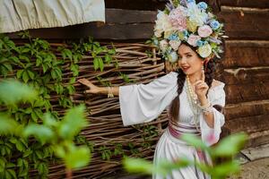 Brunette girl in a white ukrainian authentic national costume and a wreath of flowers is posing against a terrace. photo