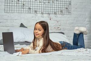 Cute little girl girl feeling amusing while watching cartoons on a laptop sitting on bed photo