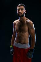 Handsome athletic guy in a red shorts on a black background. The boxer is fetching his breath after practicing hooks and blows. photo